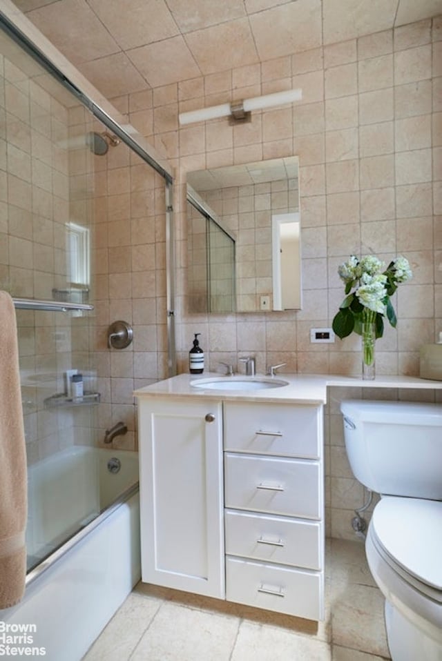 bathroom featuring tile patterned flooring, toilet, vanity, tile walls, and combined bath / shower with glass door