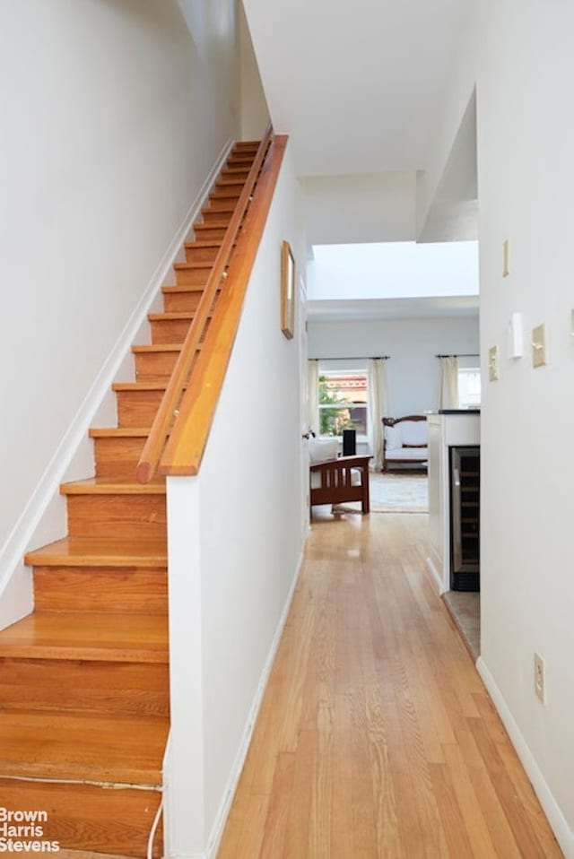 stairway with beverage cooler, a fireplace, wood finished floors, and baseboards