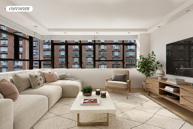 living area with a tray ceiling, visible vents, and wood finished floors