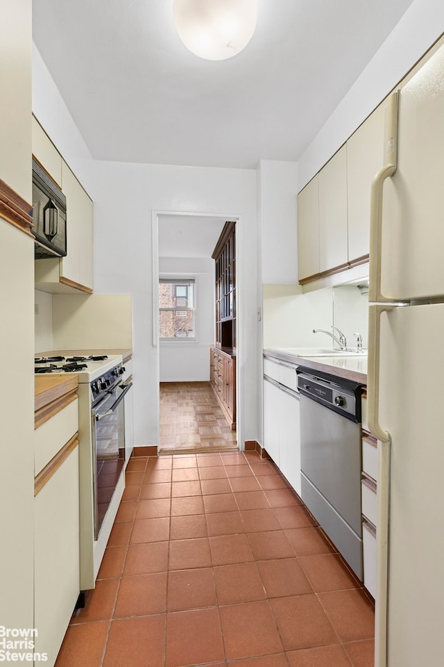 kitchen with white appliances, baseboards, light countertops, dark tile patterned floors, and a sink