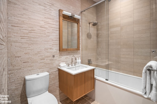 full bathroom with tile walls, combined bath / shower with glass door, vanity, and toilet