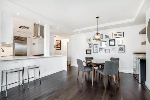 dining room with recessed lighting, a raised ceiling, and dark wood-style flooring