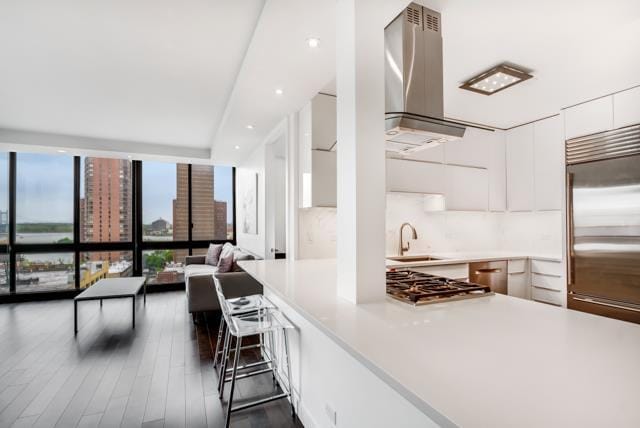 kitchen featuring stainless steel appliances, a sink, light countertops, wall chimney range hood, and modern cabinets