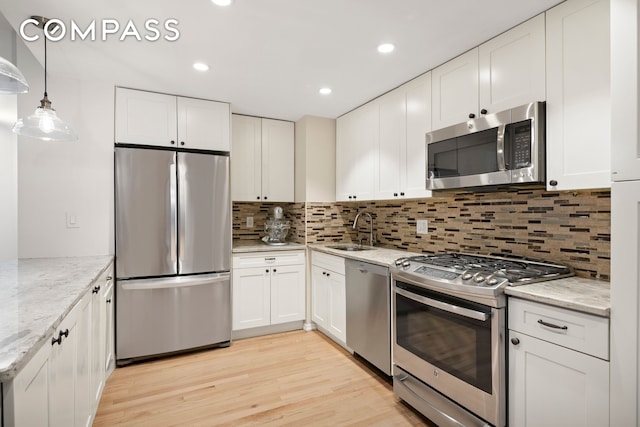 kitchen featuring a sink, white cabinets, light wood-style floors, appliances with stainless steel finishes, and decorative backsplash