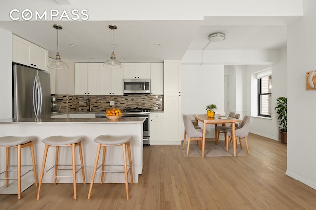 kitchen featuring white cabinetry, appliances with stainless steel finishes, light wood finished floors, a kitchen bar, and tasteful backsplash