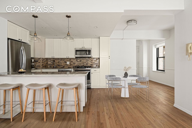 kitchen featuring backsplash, a breakfast bar, light stone counters, appliances with stainless steel finishes, and a peninsula