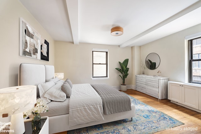 bedroom featuring beam ceiling, multiple windows, light wood-type flooring, and baseboards