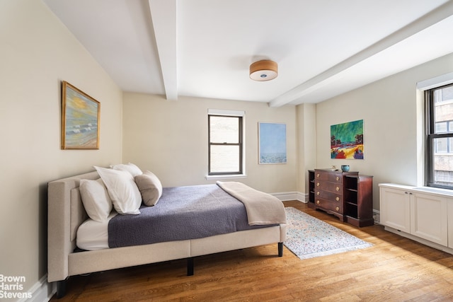 bedroom with light wood-style floors, multiple windows, baseboards, and beamed ceiling