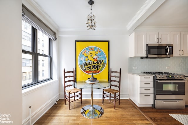 interior space with appliances with stainless steel finishes, white cabinets, light wood finished floors, a notable chandelier, and ornamental molding