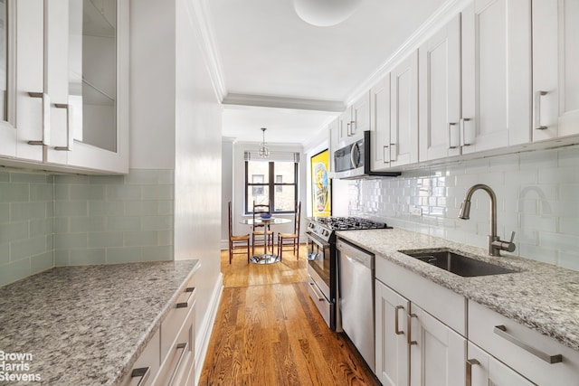 kitchen featuring crown molding, white cabinets, a sink, stainless steel appliances, and decorative backsplash