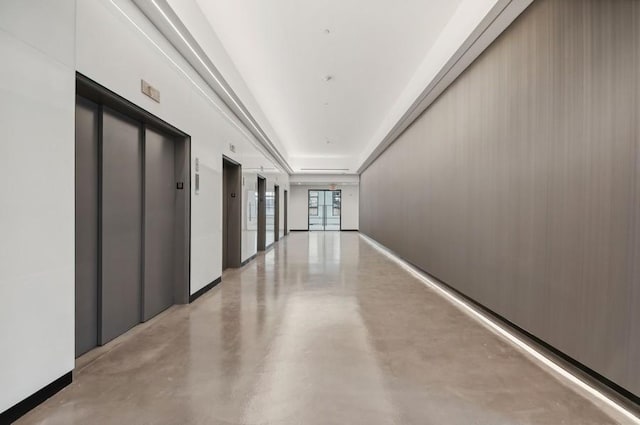 hallway with elevator, finished concrete flooring, and baseboards