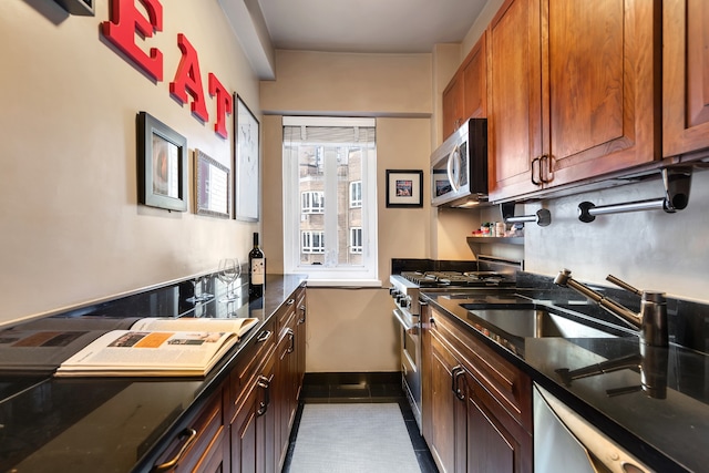 kitchen with baseboards, dark stone countertops, stainless steel appliances, dark tile patterned floors, and a sink