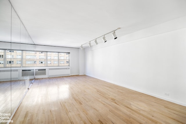 unfurnished living room featuring radiator, rail lighting, wood finished floors, and baseboards