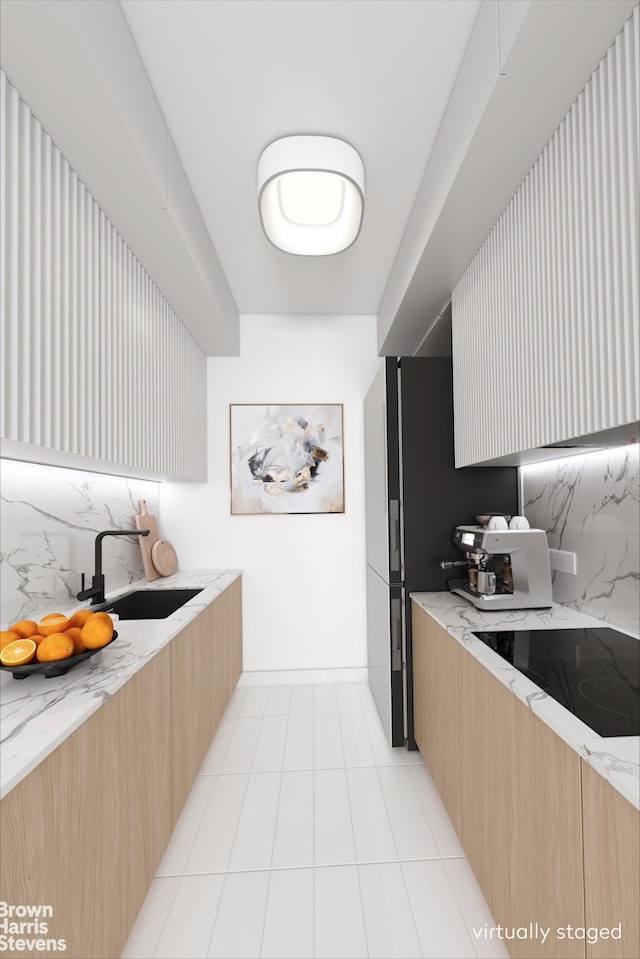 kitchen featuring backsplash, a sink, light stone countertops, and black electric cooktop