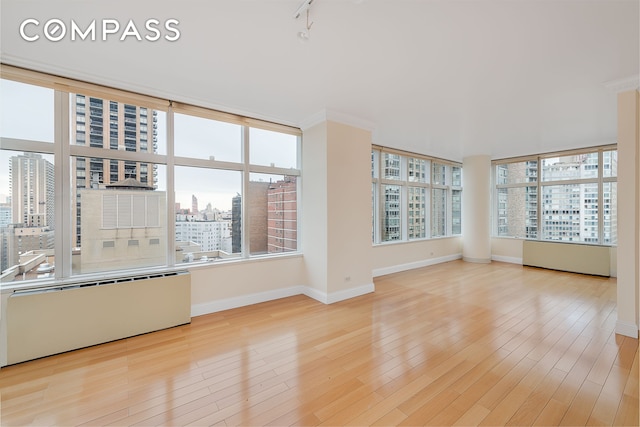 empty room with a view of city, wood finished floors, baseboards, and a wealth of natural light