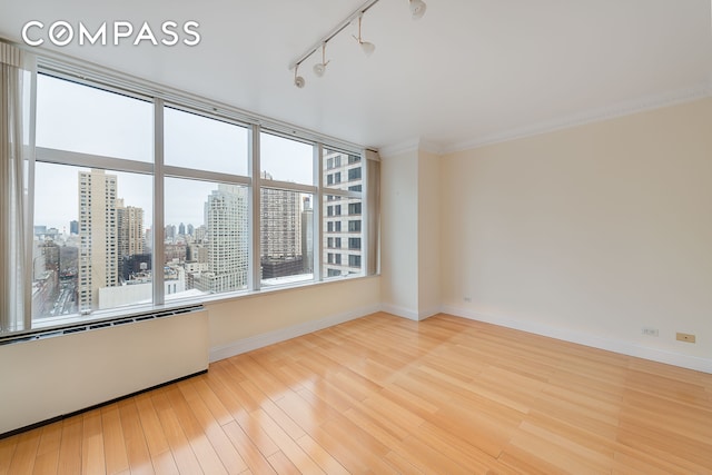 unfurnished room with a view of city, wood finished floors, rail lighting, crown molding, and baseboards