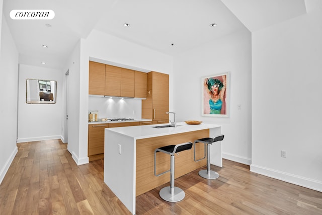 kitchen featuring visible vents, a breakfast bar, light wood-style flooring, a sink, and light countertops