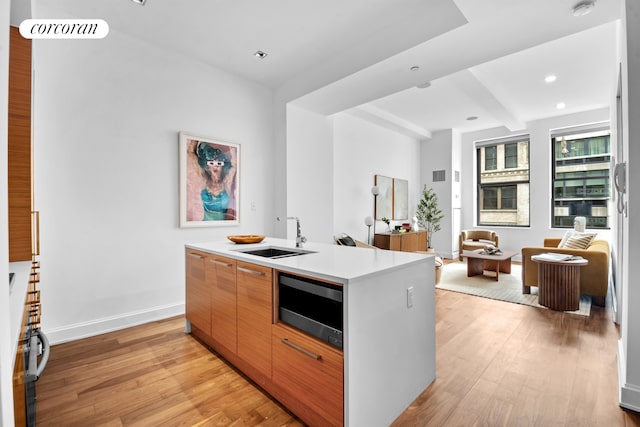 kitchen featuring modern cabinets, a center island with sink, a sink, stainless steel microwave, and light wood-style floors