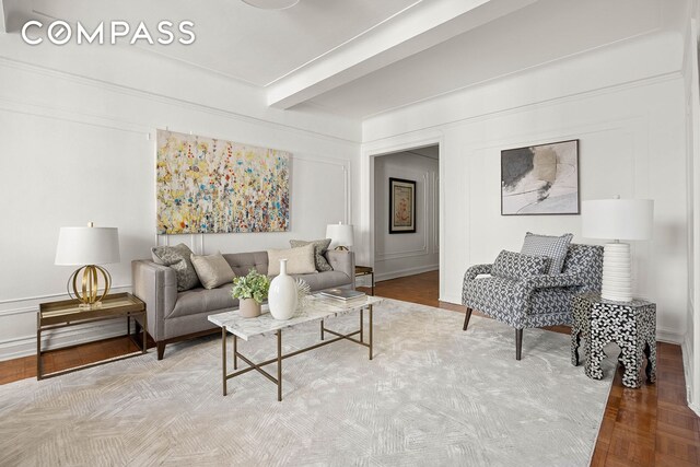 living area with beam ceiling, a decorative wall, and wood finished floors