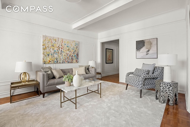 living room featuring a decorative wall, wood finished floors, and beamed ceiling