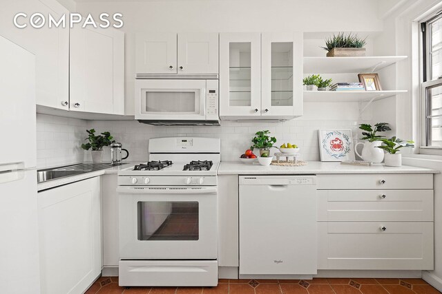 kitchen featuring white appliances, glass insert cabinets, light countertops, white cabinetry, and backsplash