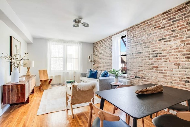 sitting room with brick wall, a wealth of natural light, and light wood-style floors