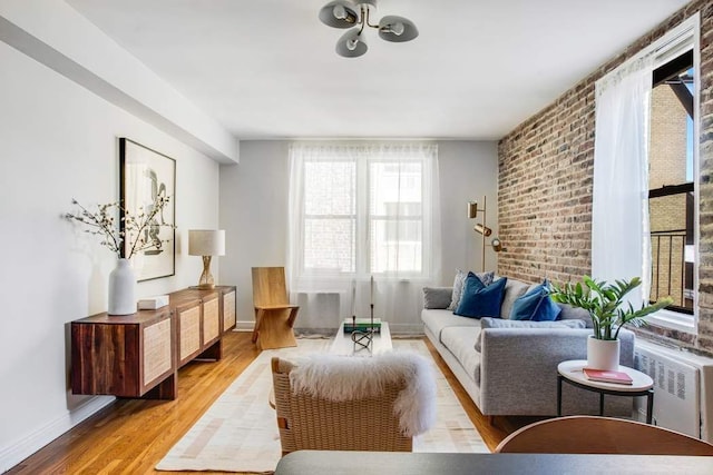 living room with radiator, light wood-style floors, brick wall, and baseboards