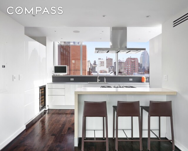 kitchen featuring wine cooler, island range hood, dark wood-type flooring, a sink, and a kitchen breakfast bar