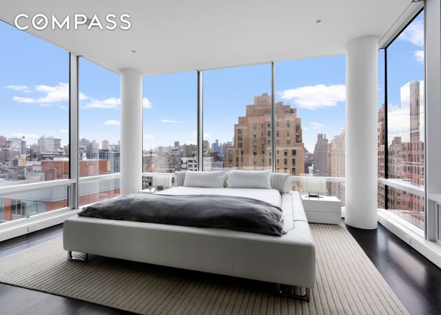 bedroom featuring a view of city, floor to ceiling windows, and wood finished floors