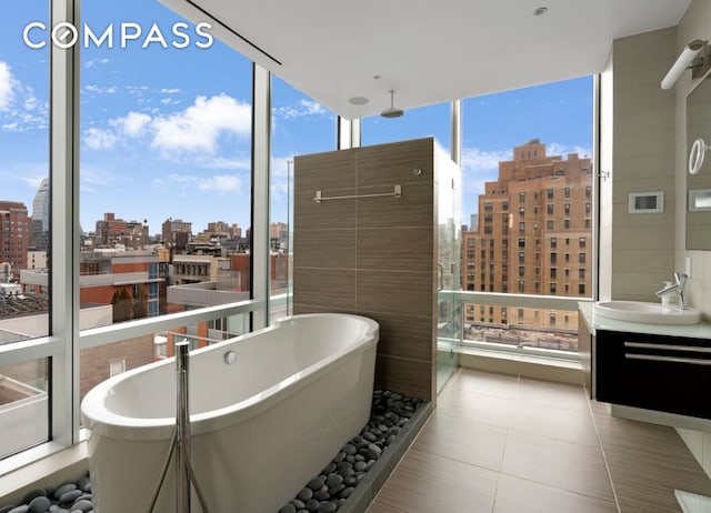 bathroom with a city view, tile patterned floors, vanity, a soaking tub, and floor to ceiling windows