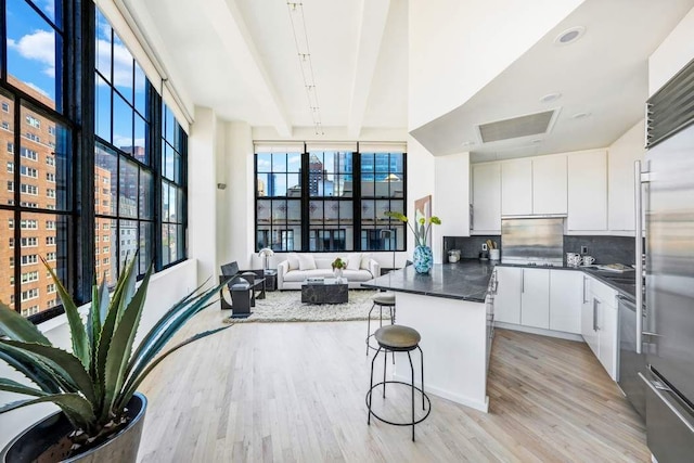 kitchen featuring dark countertops, a kitchen breakfast bar, light wood-type flooring, white cabinetry, and backsplash