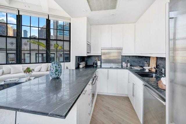 kitchen with stainless steel appliances, white cabinets, a sink, and a peninsula