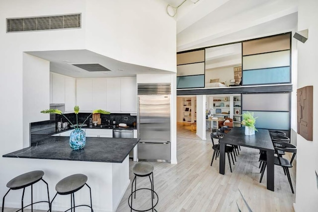 kitchen with stainless steel appliances, dark countertops, visible vents, a peninsula, and a kitchen bar