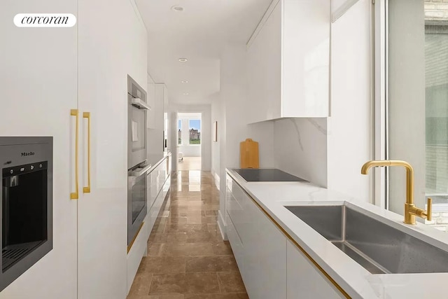 kitchen with black electric stovetop, a sink, white cabinets, light countertops, and modern cabinets