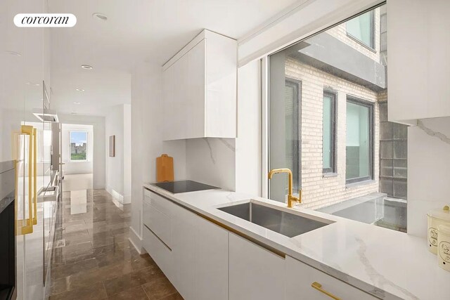 kitchen featuring light countertops, white cabinets, a sink, modern cabinets, and black electric cooktop