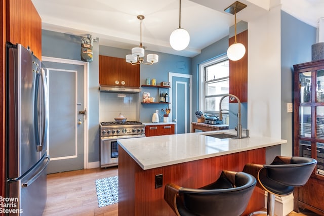 kitchen featuring brown cabinets, stainless steel appliances, a sink, a peninsula, and under cabinet range hood