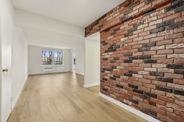 unfurnished living room with baseboards, radiator, brick wall, and light wood finished floors