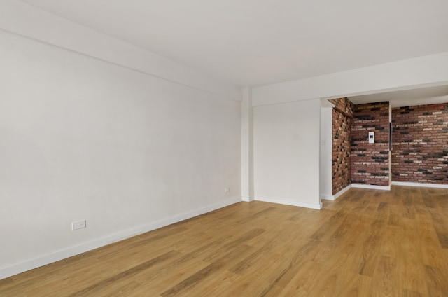 unfurnished room with light wood finished floors, brick wall, and baseboards