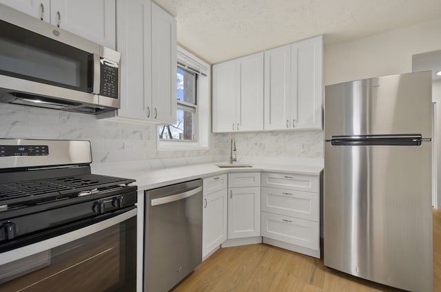 kitchen with appliances with stainless steel finishes, white cabinetry, light countertops, and a sink