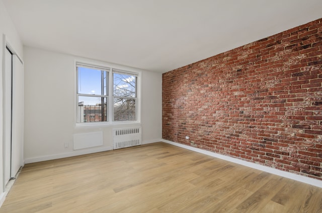 empty room with brick wall, radiator heating unit, baseboards, and light wood-style flooring