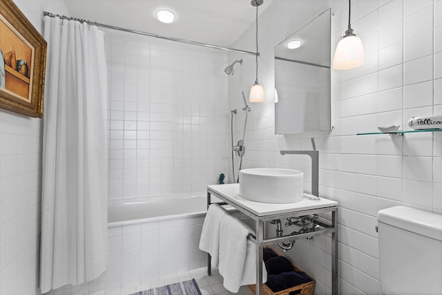 bathroom with a sink, tiled shower / bath, toilet, and tile walls