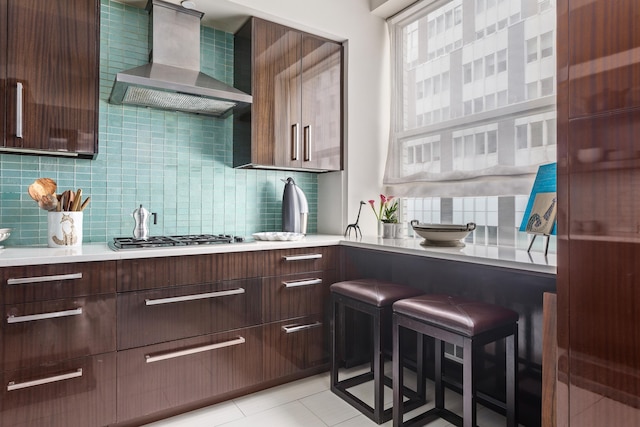 kitchen featuring decorative backsplash, modern cabinets, light countertops, wall chimney range hood, and stainless steel gas stovetop