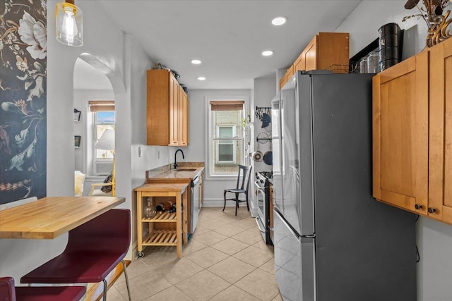 kitchen with a sink, stainless steel appliances, arched walkways, light tile patterned floors, and recessed lighting