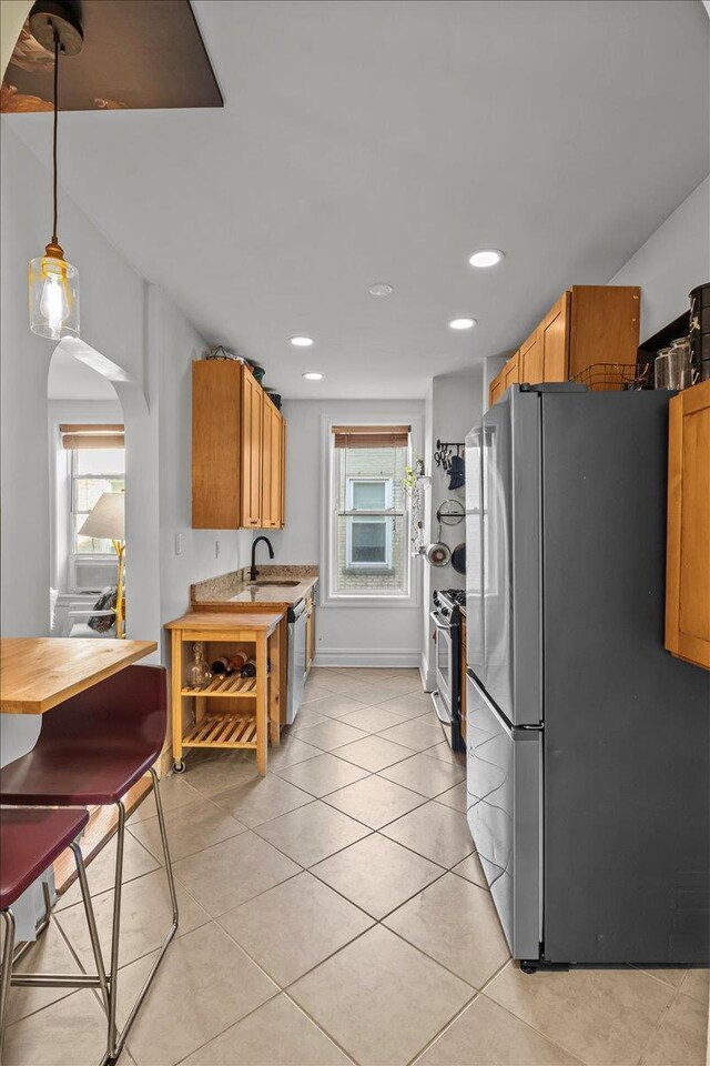kitchen featuring stainless steel appliances, arched walkways, light tile patterned floors, a sink, and light countertops