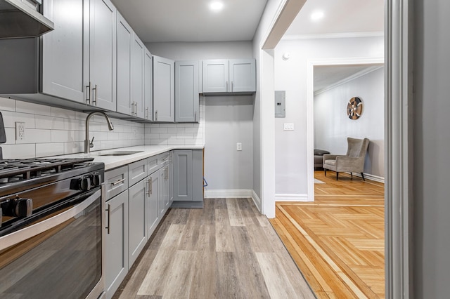 kitchen with tasteful backsplash, gray cabinetry, stainless steel range with gas cooktop, under cabinet range hood, and a sink