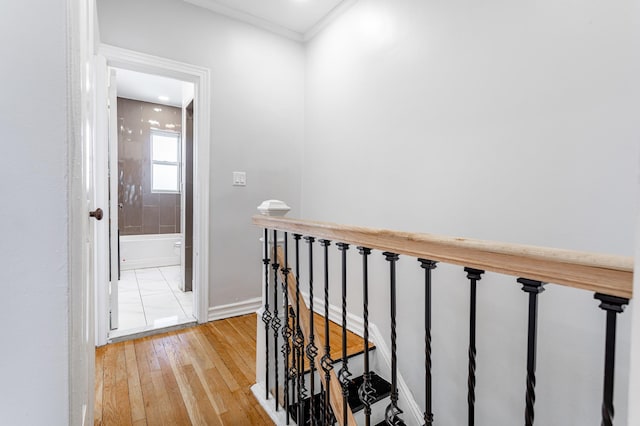 corridor featuring ornamental molding, an upstairs landing, light wood-style floors, and baseboards