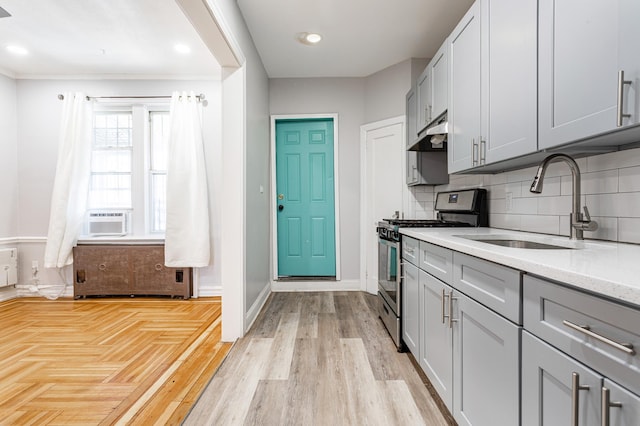 kitchen with under cabinet range hood, gray cabinetry, stainless steel gas range, and a sink