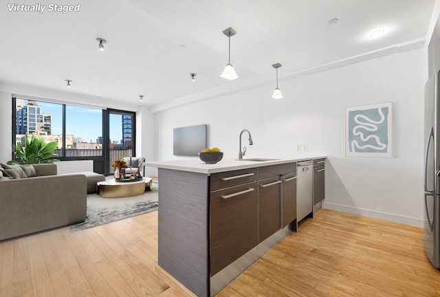 kitchen with hanging light fixtures, light wood-style floors, open floor plan, a sink, and a peninsula