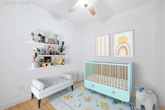 bedroom with a nursery area, ceiling fan, baseboards, and wood finished floors