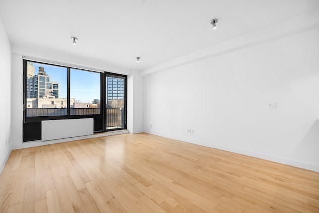 spare room with a view of city, light wood finished floors, and baseboards